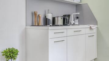 Una cocina blanca con microondas integrado, cafetera y una pequeña planta en maceta.