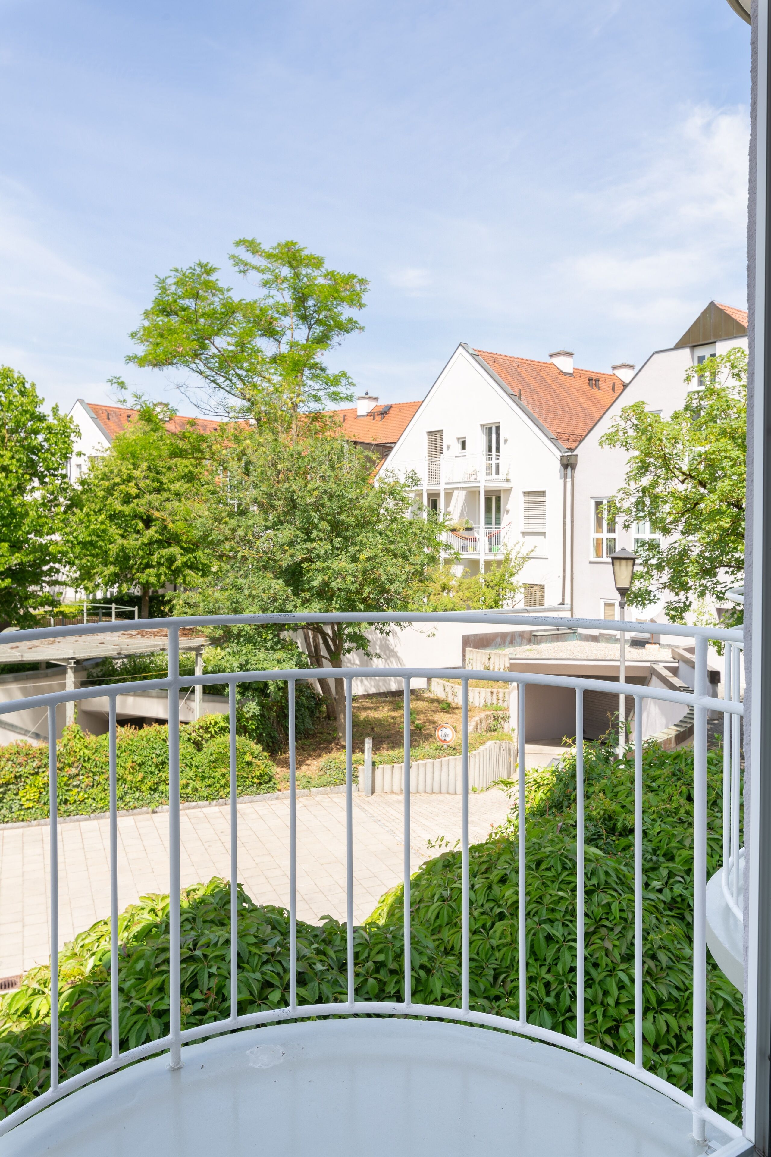 A balcony with white railings overlooking a residential area with houses and greenery.