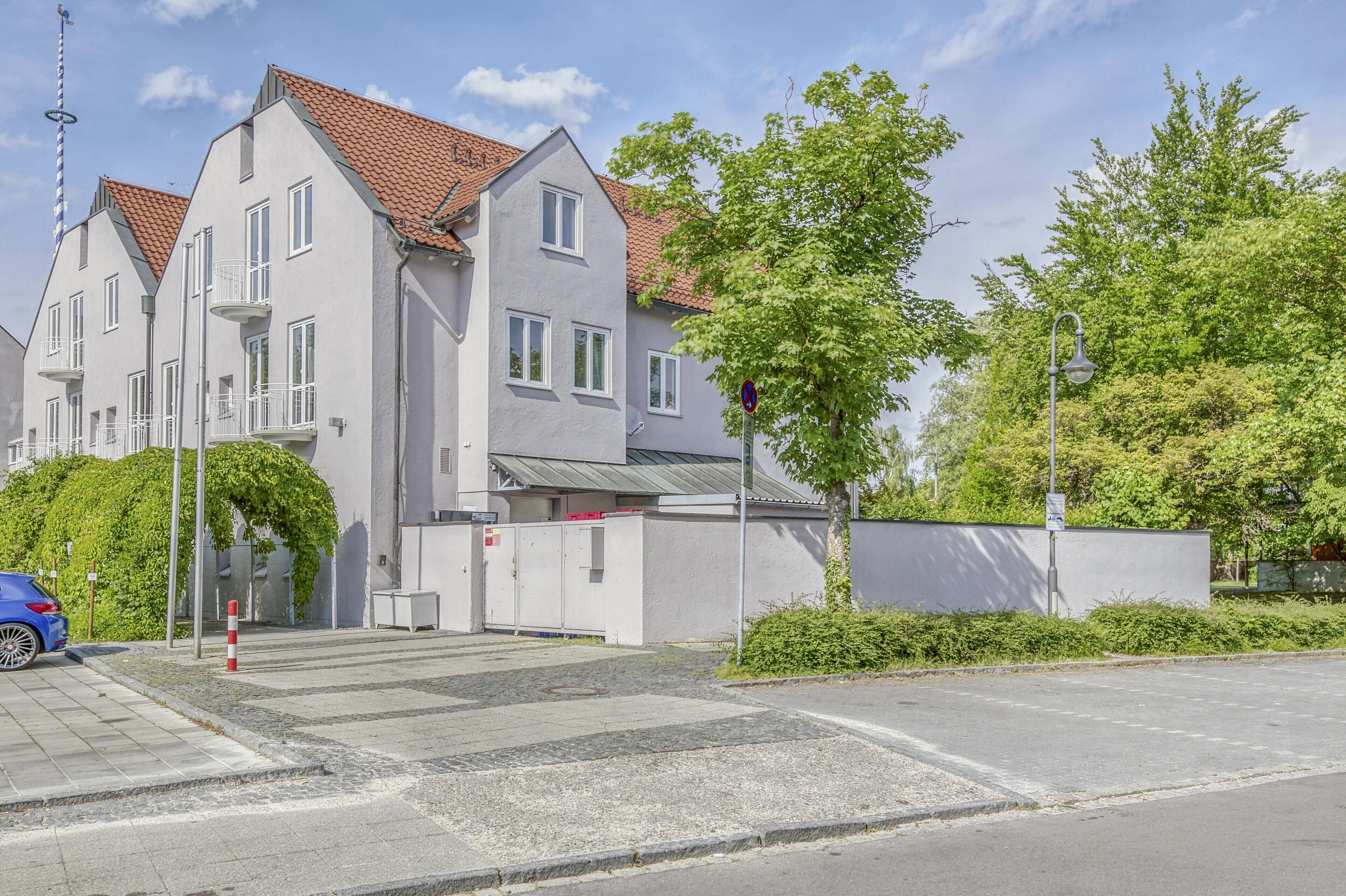 A multi-story building with a red-tiled roof, a gated entrance, and a parking area.