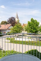 A view of a town square with a church steeple, a roundabout, and surrounding greenery.