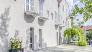 Ein modernes Gebäude mit Innenhof, das einen gepflasterten Weg und eine kleine Grünfläche mit Blumenkasten und Baum zeigt.