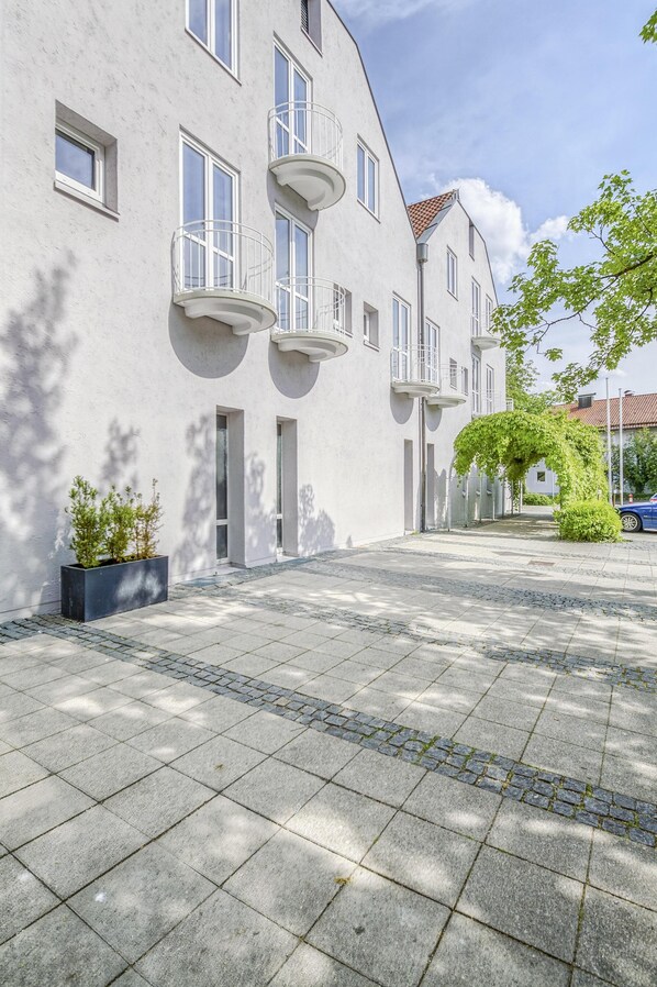 Un edificio moderno con patio, que presenta un paseo empedrado y un pequeño jardín con macetas y un árbol.