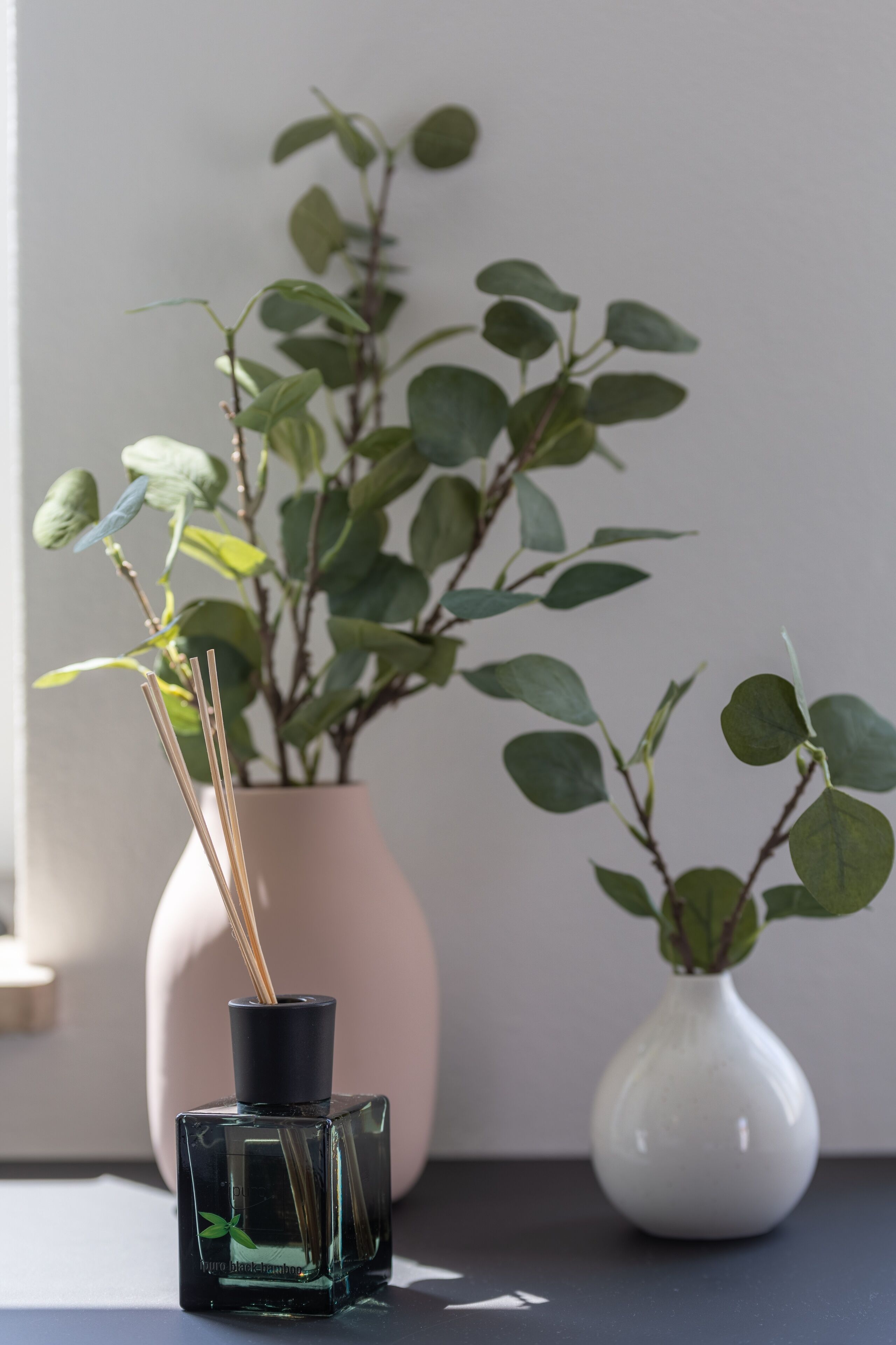 A small table with two vases, one containing a plant and the other with a reed diffuser.