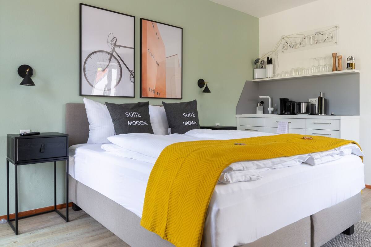 Une chambre moderne comprenant un lit, des tables de chevet, un bureau et un coin cuisine.
