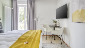 Ein Hotelzimmer mit einem Bett, einem Schreibtisch, einem Sessel, einem Fernseher und einem Fenster mit Vorhängen.