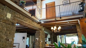 A rustic interior with a stone wall, wooden beams, a balcony with a metal railing, and a chandelier. - CAL SERRA-Rural house (Alentorn)