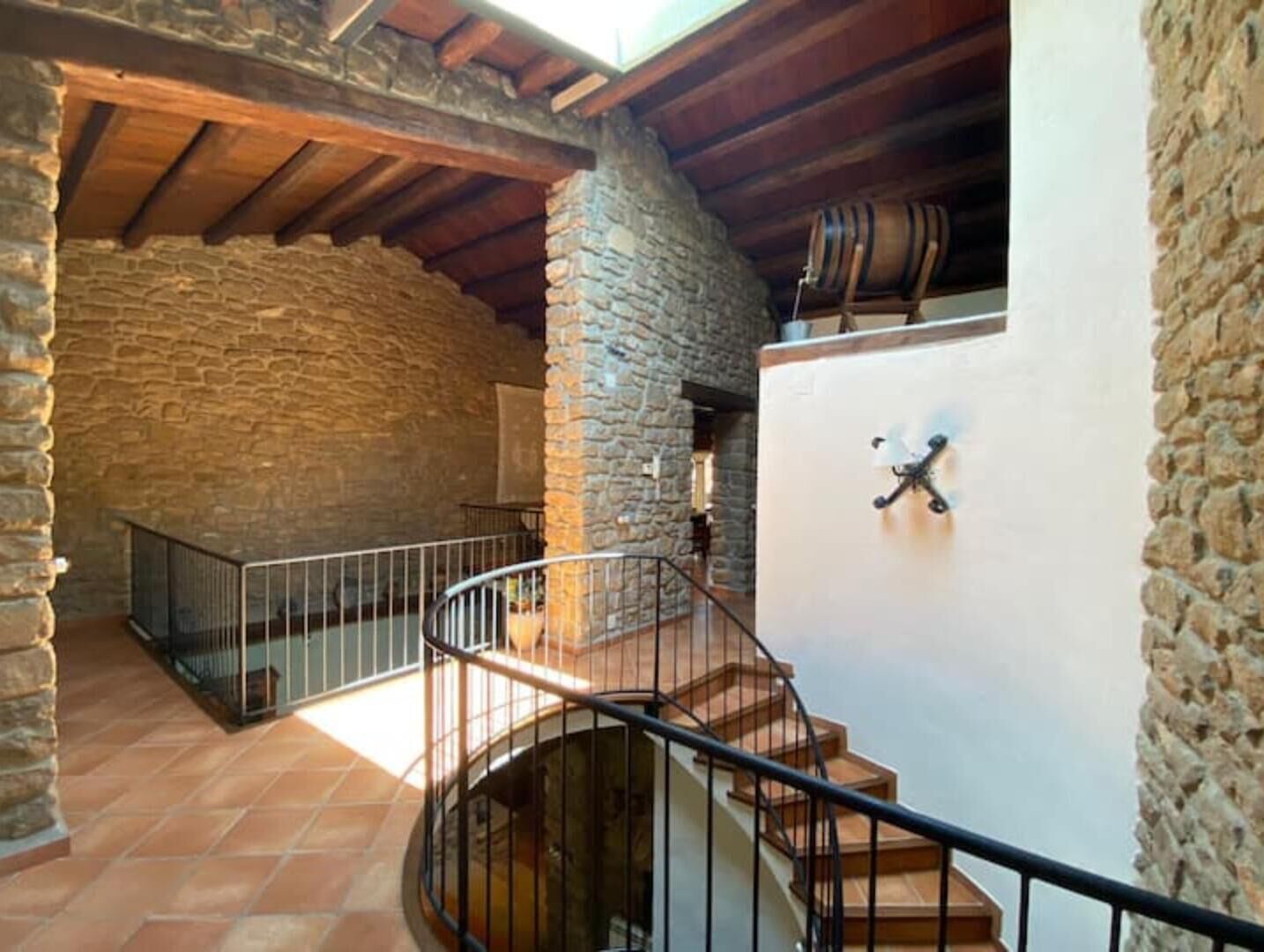 A stone-walled room with a spiral staircase and a rustic wooden ceiling.