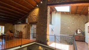 A spacious interior with a stone wall, wooden beams, a balcony, and a staircase. - CAL SERRA-Rural house (Alentorn)