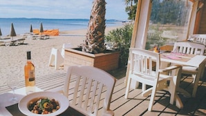 Un restaurante frente a la playa con terraza al aire libre, una cubierta de madera y vistas a la playa y el océano.