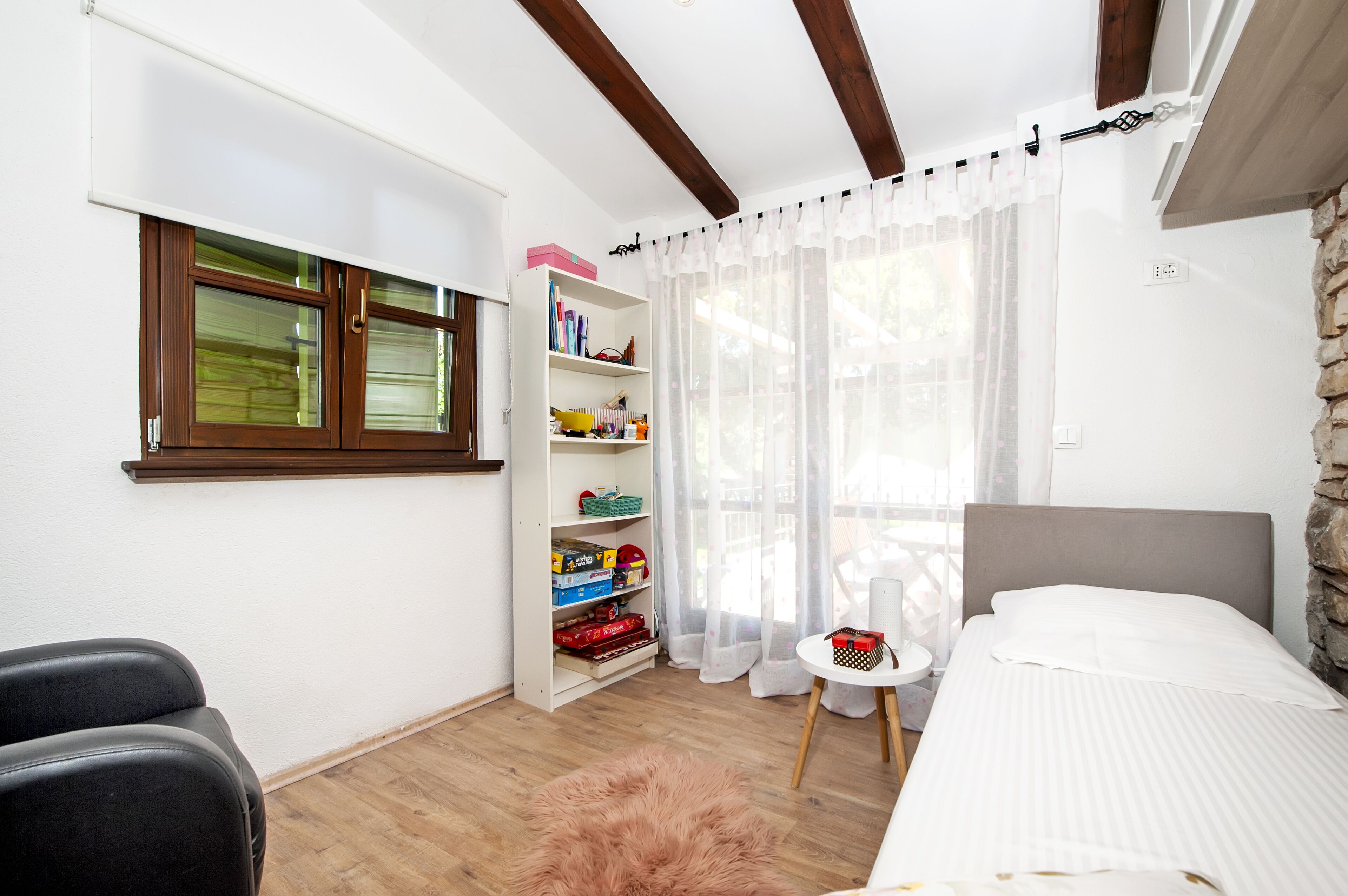 Une chambre à coucher avec un lit, une armoire blanche, une petite table ronde, une chaise et une fenêtre avec des rideaux.