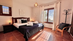 A hotel room with a bed, bedside lamps, a chair, and a window with curtains. - Andalusian style villa with stunning views. PAX 6. FREE WIFI (Tarifa)