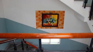 A staircase with a wooden handrail and a tiled wall with a framed painting. - Sen Vang Guest House (Nha Trang)