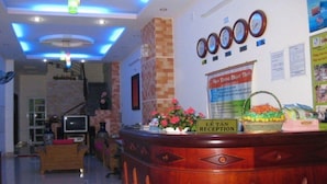 A reception area with a wooden reception desk, a clock, and a sign that reads "LE TRAVAIL RÉCEPTION". - Sen Vang Guest House (Nha Trang)