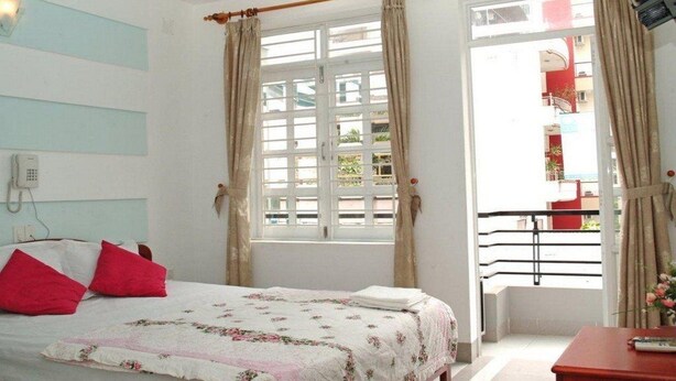 A bedroom with a bed, a window with curtains, a balcony, and a phone on the wall. - Sen Vang Guest House (Nha Trang)