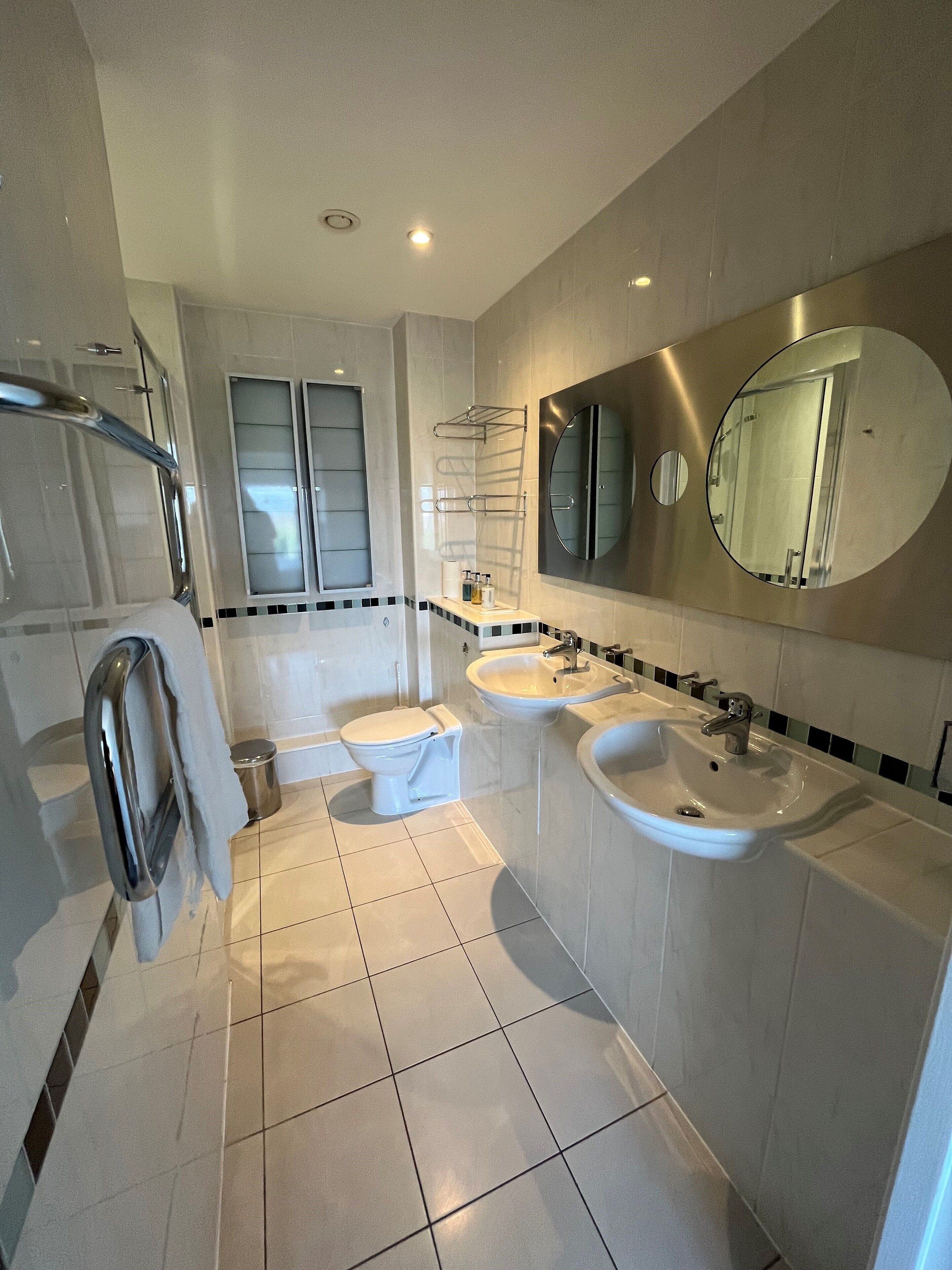 A modern bathroom with a toilet, bidet, two sinks, and a mirror.