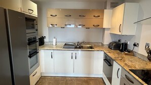 A modern kitchen with white cabinets, a stainless steel refrigerator, a built-in oven, a sink, and a stove.