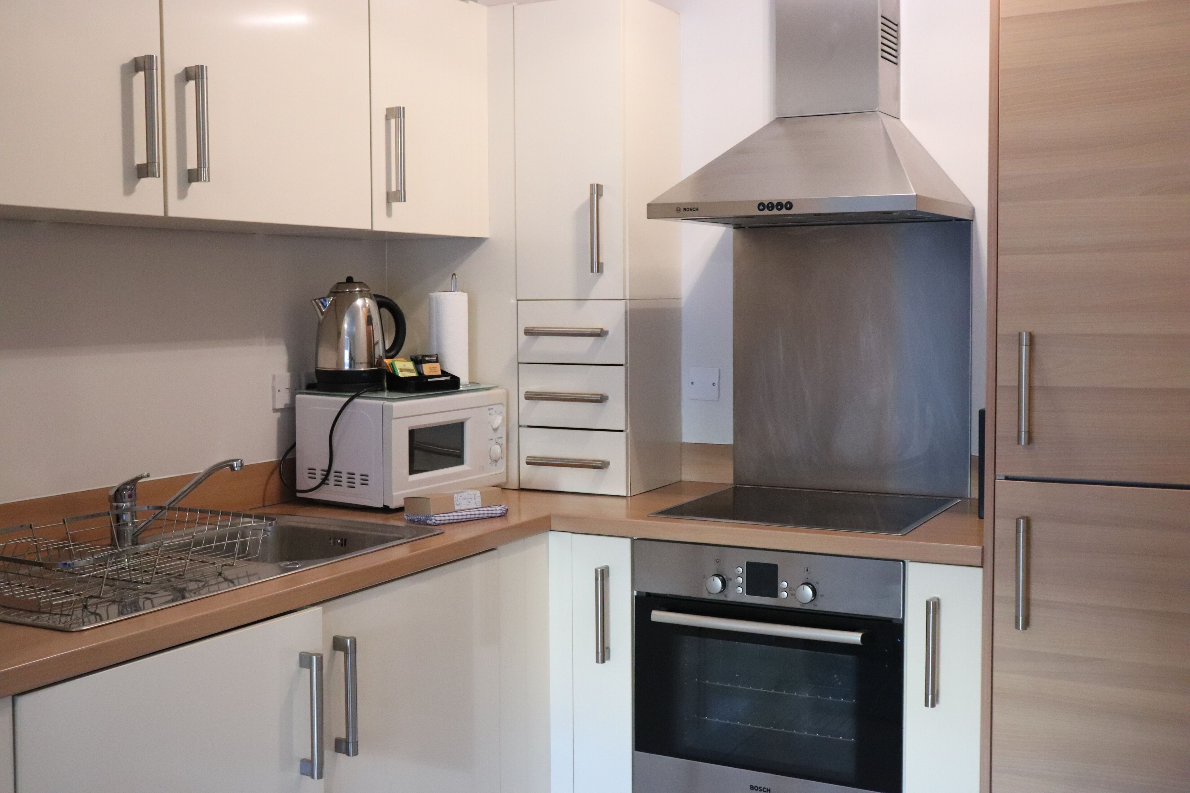 A modern kitchen with white cabinets, stainless steel appliances, and a wooden countertop.