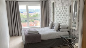 A bedroom with a large bed, a glass table, and a view of a cityscape.