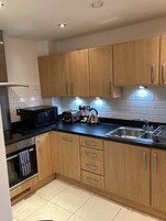 A modern kitchen with wooden cabinets, a black countertop, a microwave, a kettle, a toaster, and a sink.