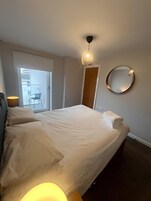 A hotel room with a bed, bedside lamps, a round mirror, and a view of the outside balcony.