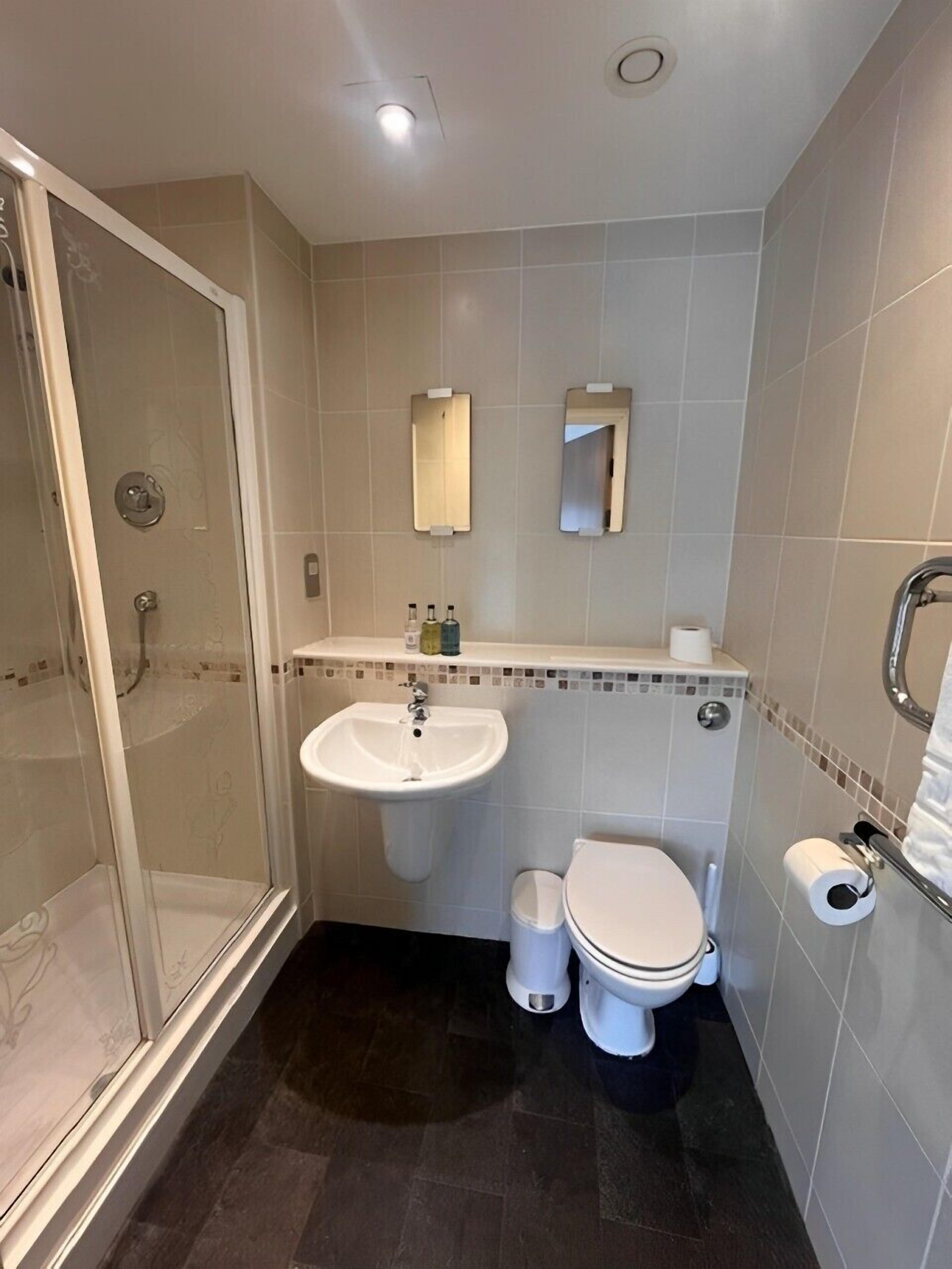 Een badkamer met een douchecabine van glas, een wastafel, toilet en een spiegel.