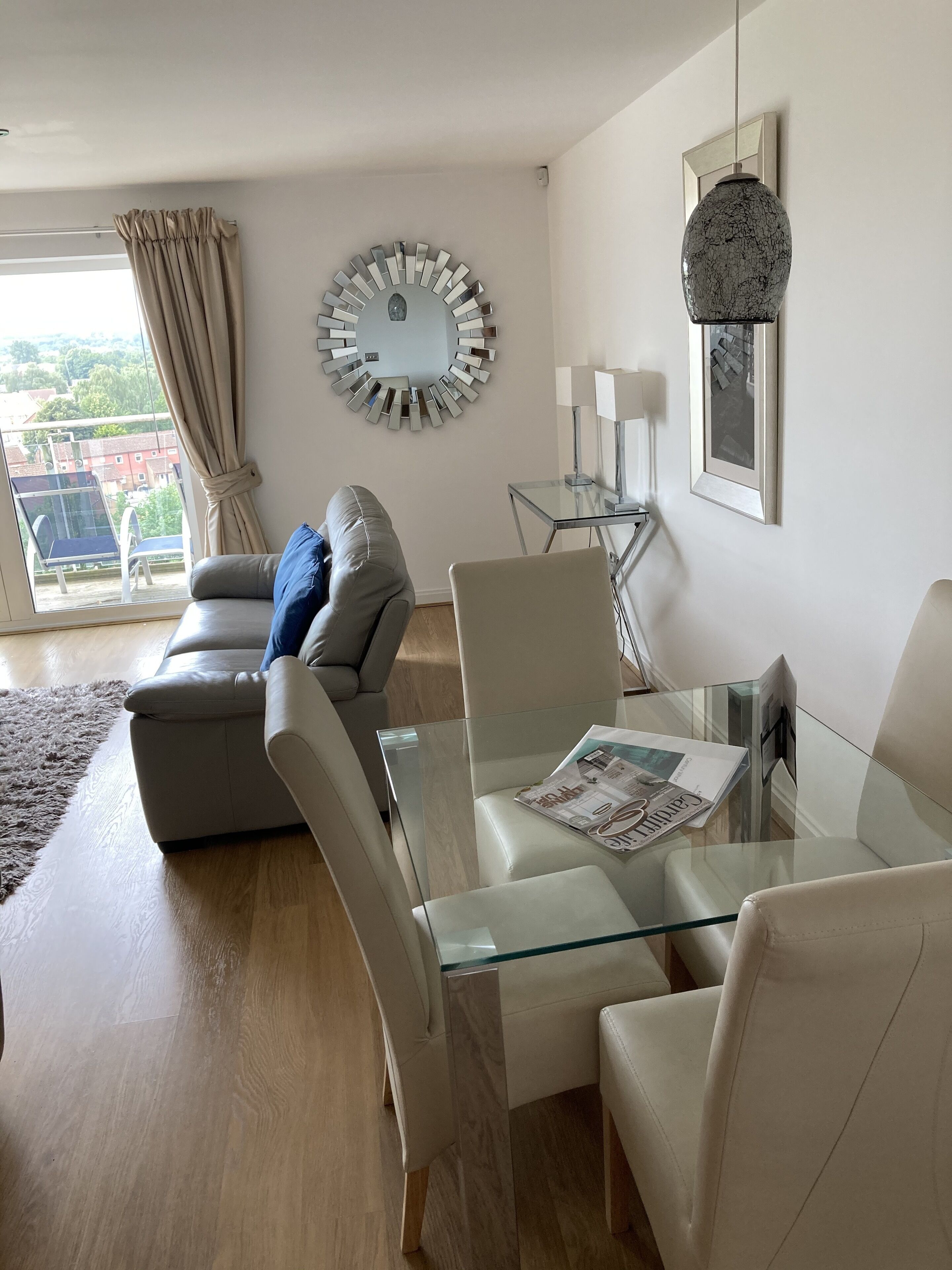 A modern living room with a glass coffee table, leather sofas, and a large mirror on the wall.