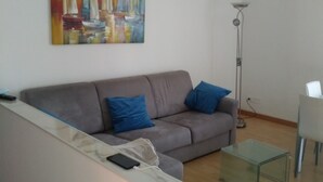 A modern living room with a grey sofa, blue cushions, a glass coffee table, and a painting of sailboats on the wall. - Quiet room in new apartment (Verona)