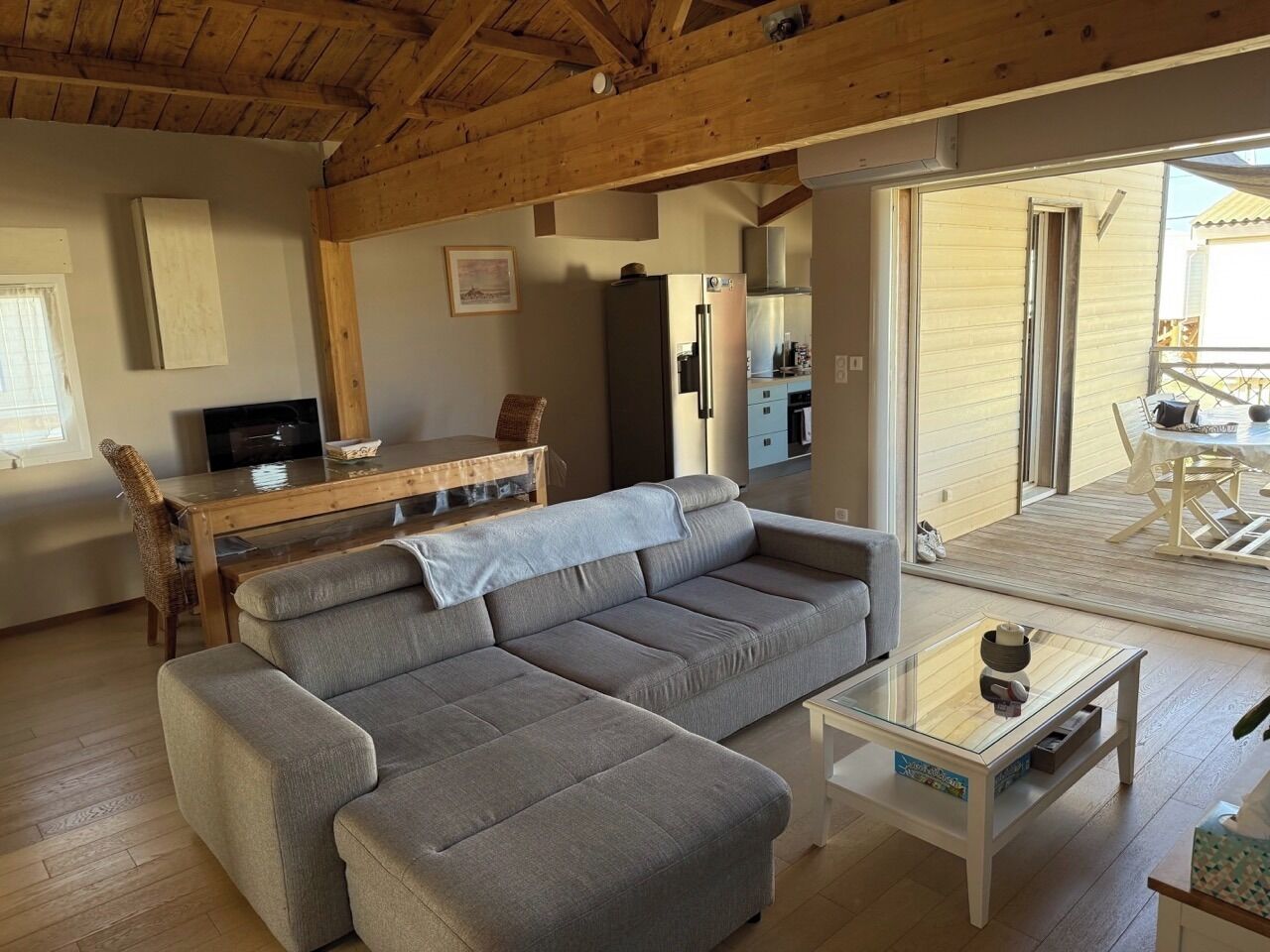 Een woonkamer met een grijze bank, een glazen salontafel en een houten eettafel met stoelen.