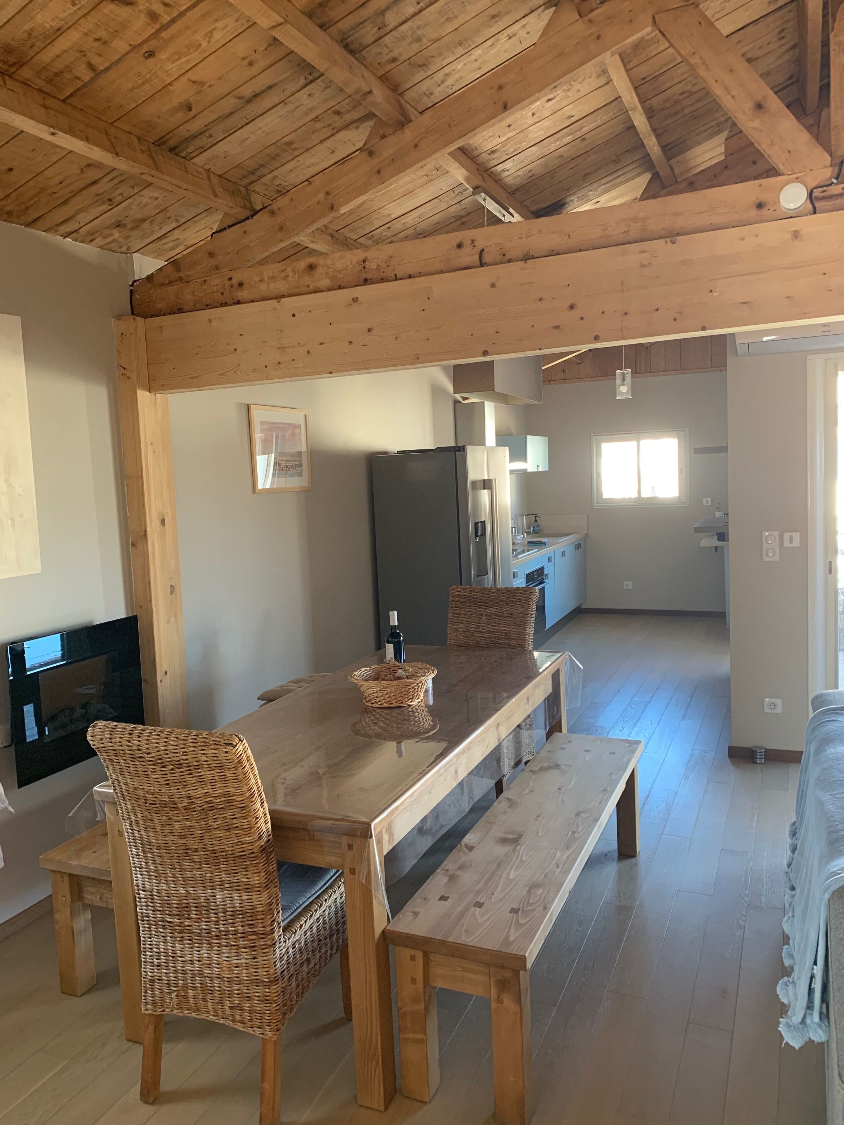 Ruime eethoek met een houten tafel, rieten stoelen en een bankje. Achtergrond toont een moderne keuken.