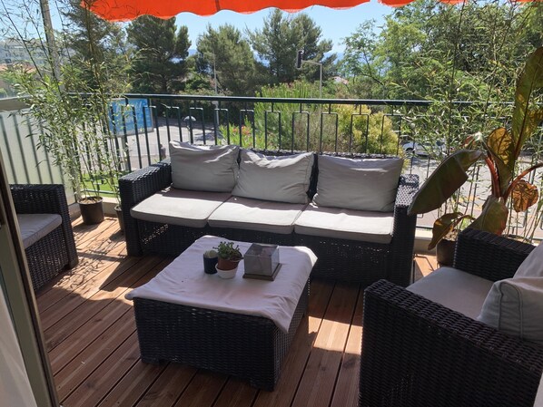 A balcony with wicker furniture, including a sofa and a table with a plant. - Sunny terrace apartment with sea view (Nice)