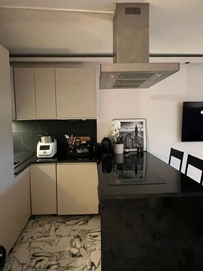 A compact kitchen with a black countertop, white cabinets, a coffee machine, and a dining area with a black table and chairs. - Sunny terrace apartment with sea view (Nice)