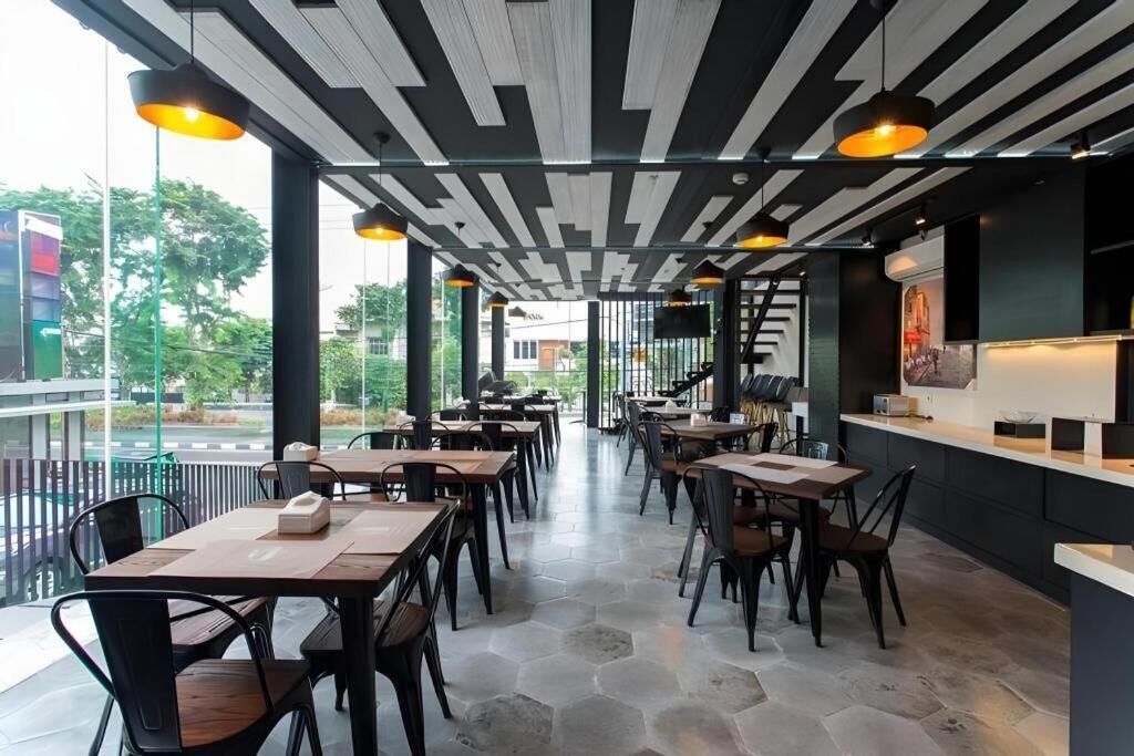 An indoor dining area with tables and chairs, a modern ceiling design, and a view through large windows.