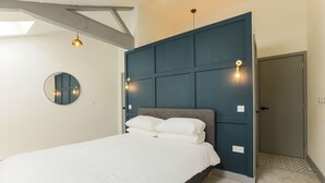 A bedroom with a bed, a wall-mounted mirror, and a door with a light switch. - Goodstay Apartments by Urban Space (Barry)