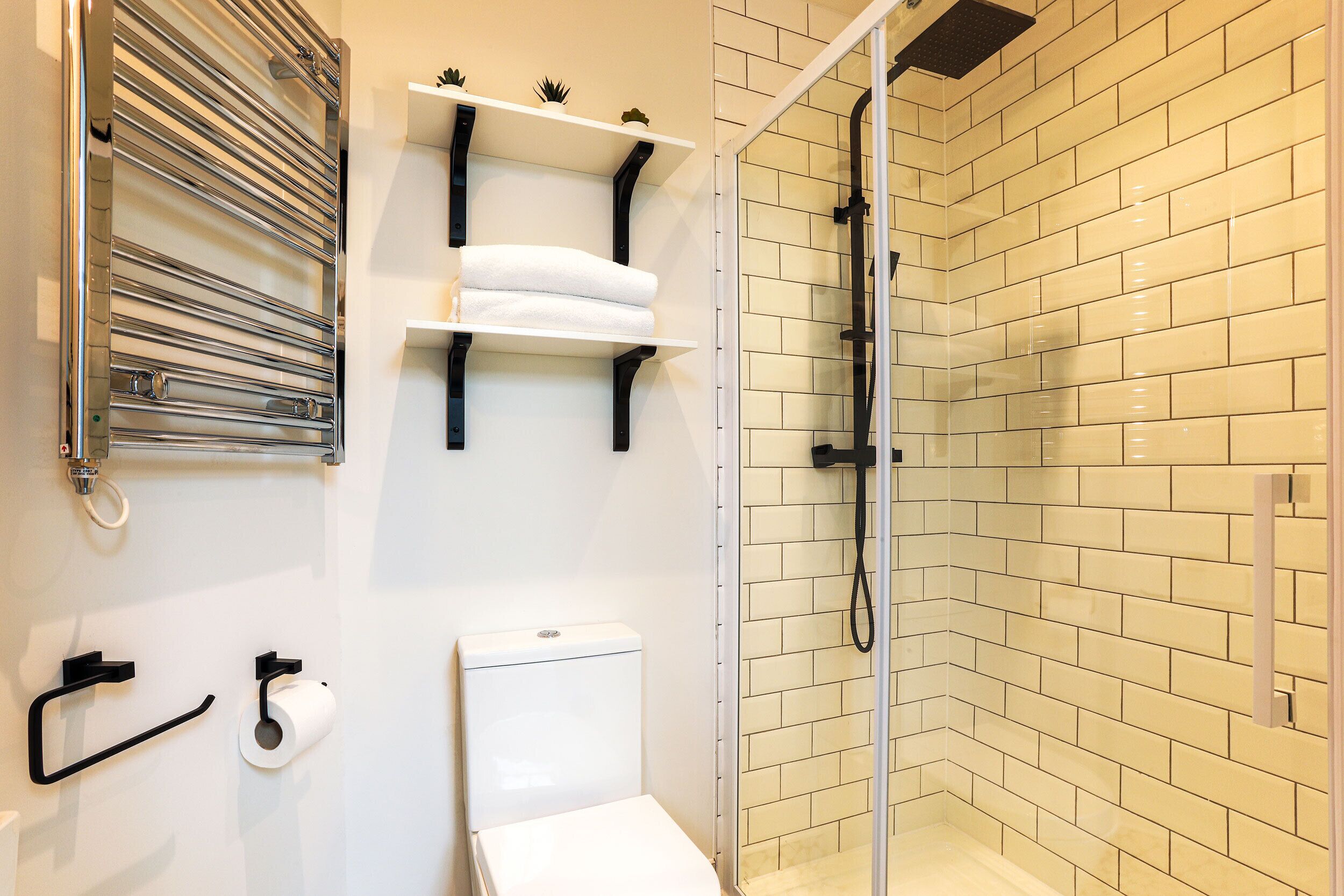 A modern bathroom with a glass-enclosed shower, white tiled walls, and a white toilet.