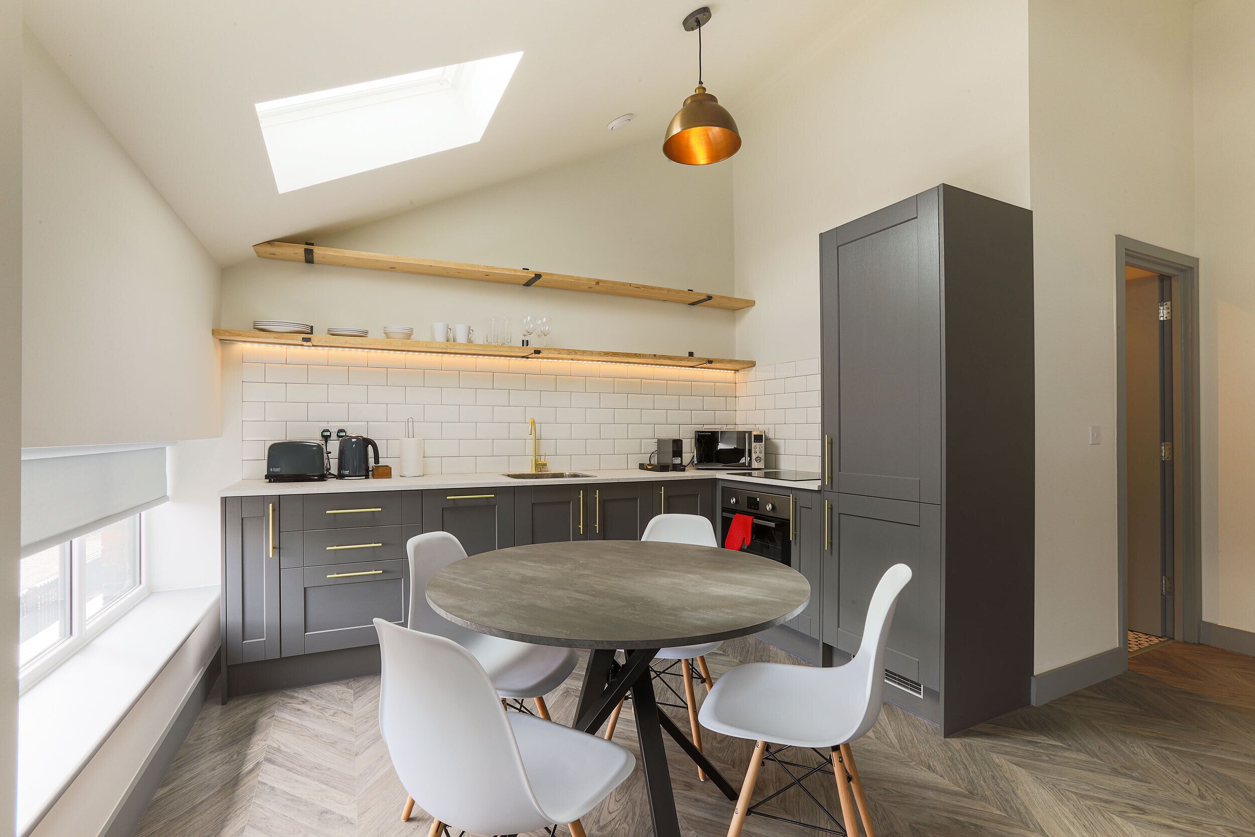 A modern kitchen with a skylight, a round dining table, and white chairs.