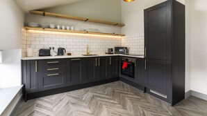 A modern kitchen with black cabinets, a herringbone-patterned floor, a skylight, and a hanging pendant light. - Goodstay Apartments by Urban Space (Barry)