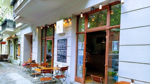 An outdoor cafe with tables and chairs, a chalkboard menu, and a door to the interior. - Quiet studio in Prenzlauer Berg near Mauerpark (Berlin)