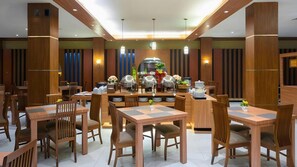 A modern dining area with wooden tables and chairs, buffet stations, and pendant lighting. - Diamond Hotel Samarinda (Samarinda)