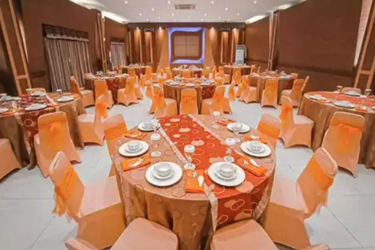 Een feestzaal met ronde tafels, oranje stoelhoezen en een centraal podium.