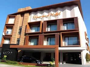 A multi-story hotel with a modern architectural design, featuring a central entrance and a parking area with a black car. - Diamond Hotel Samarinda (Samarinda)