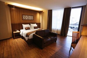 A hotel room with a bed, a sofa, a desk, and a window with curtains. - Diamond Hotel Samarinda (Samarinda)