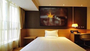 A hotel room with a large bed, a nightstand, a desk with a lamp, and a painting of a bird on the wall. - IU Hotel Bijie Weining Caohai (Bijie)