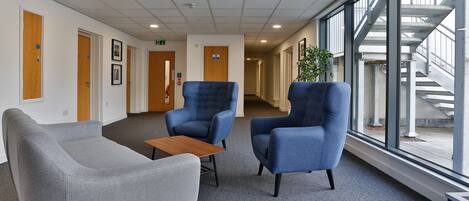 Un espace d’attente moderne avec un canapé gris, deux fauteuils bleus et une petite table en bois.