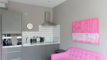 A modern kitchen with grey cabinets, a white countertop, and a pink sofa in the living area.