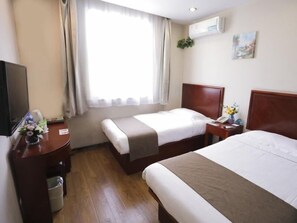 A hotel room with two beds, a TV, a desk with a vase of flowers, a window with curtains, and an air conditioning unit on the wall. - Greentree Inn Baoding Sanfeng Road Agricultural Un (Baoding)