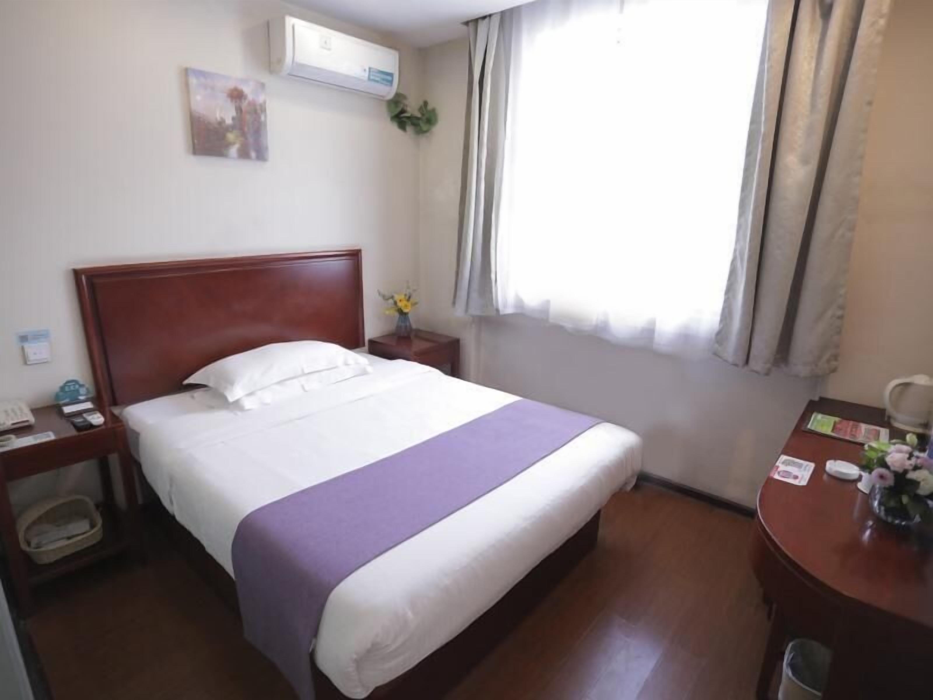 A hotel room with a bed, bedside table, and a window with curtains.