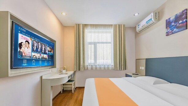 Une chambre d’hôtel comprenant un lit, un bureau, une chaise, un téléviseur fixé au mur et une fenêtre avec des rideaux.