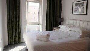 A hotel room with a bed, a window, curtains, a bedside table, a lamp, and a framed picture on the wall. - Quayside by Urban Space (Cardiff)