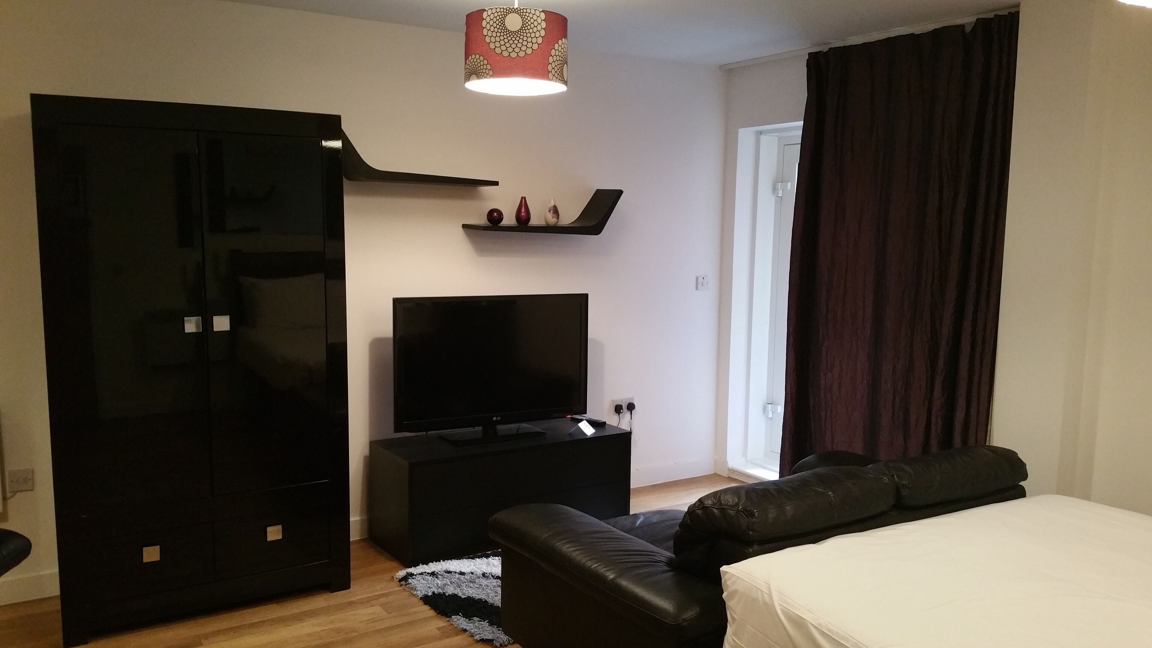 A modern hotel room with a flat-screen TV, a black sofa, a bed, and a wardrobe.