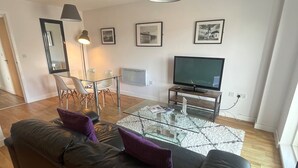 A modern living room with a black leather sofa, a glass coffee table, a flat-screen TV, and framed pictures on the wall. - Quayside by Urban Space (Cardiff)
